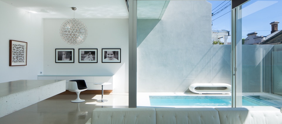Minimalist white living area with concrete floors overlooking a small in ground pool with floor to ceiling windows Melbourne