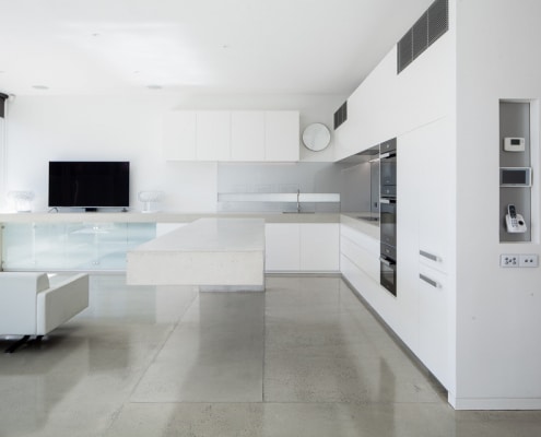 Minimalist white kitchen and lounge space with polished concrete floors in South Yarra
