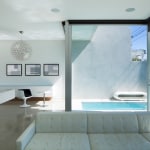 Minimalist white living area with concrete floors overlooking a small in ground pool with floor to ceiling windows