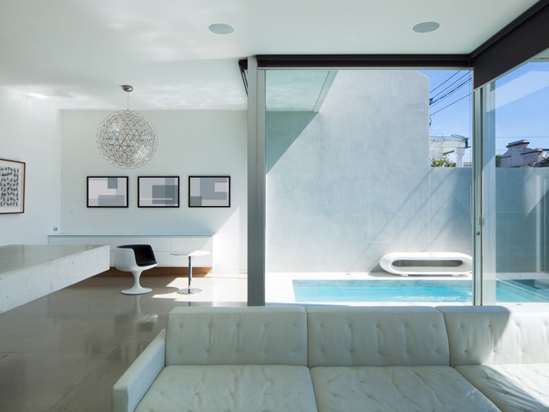 Minimalist white living area with concrete floors overlooking a small in ground pool with floor to ceiling windows